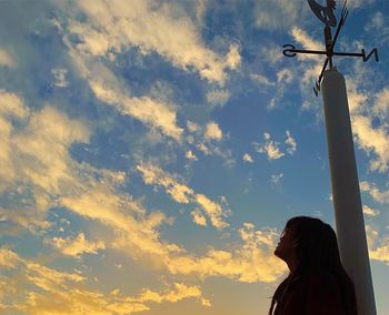 Low angle view of silhouette woman standing by weather vane against sky