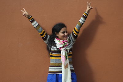 Woman with arms raised standing against wall