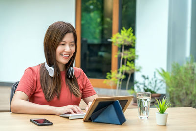 Portrait of smiling young woman using phone while sitting on table