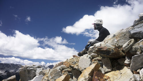 Side view of man sitting on rock against sky