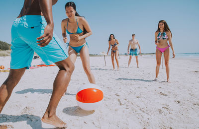 Friends playing with ball at beach against sky