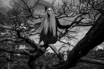 Woman sitting on bare tree in forest