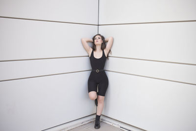 Full body of young woman in black suit and shoes looking at camera while standing in in fashion pose