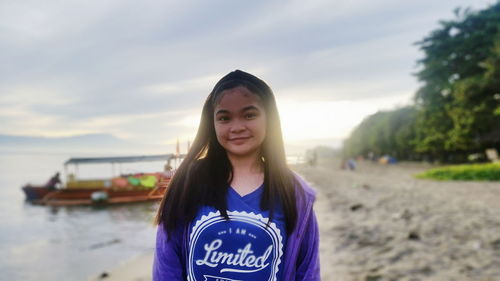 Portrait of young woman standing on beach against sky