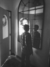 Rear view of boy standing by window at home