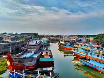 Fishing boats moored at harbor against sky