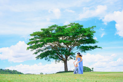 Woman standing by tree on field against sky