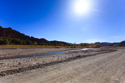 Scenic view of road by field against clear blue sky