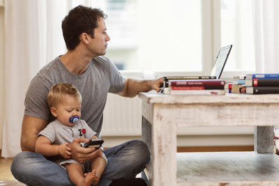 Man using laptop while holding baby boy at home