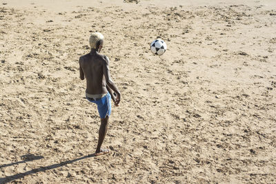 Rear view of boy playing with ball on beach