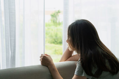 Side view of woman sitting on bed at home