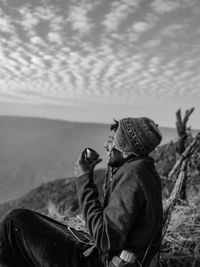 Man holding a glass and wearing a cap against sky