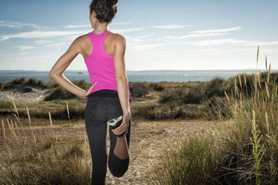 Woman looking out to sea while doing a leg stretch and keeping fit