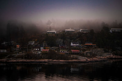 Scenic view of lake by buildings against sky at dusk