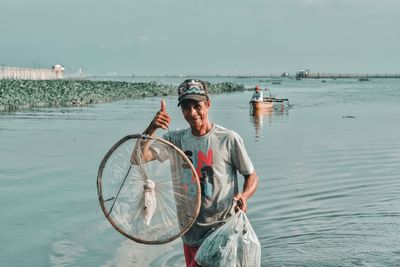 Man working on fishing boat at sea against sky