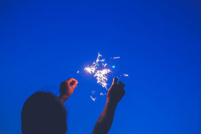 Low angle view of hand holding sparkler against clear blue sky