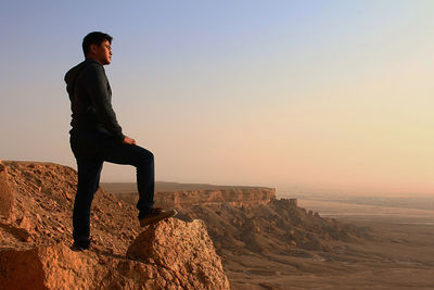 Man standing on rock against sky during sunset