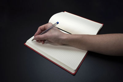 Close-up of hand holding book against black background