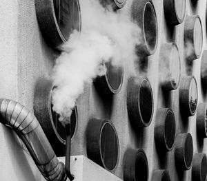 Low angle view of smoke stack emitting pollution against windows