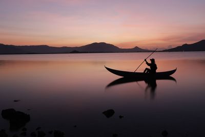 Silhouette person in lake against sky during sunset