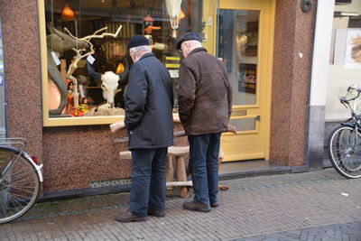 Rear view of men standing on street and looking at retail display