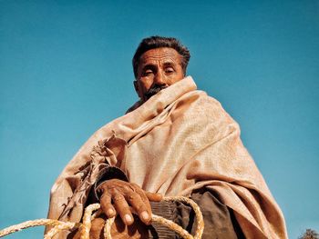 Low angle portrait of man wearing shawl against clear blue sky