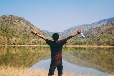 Rear view of man standing by lake against sky