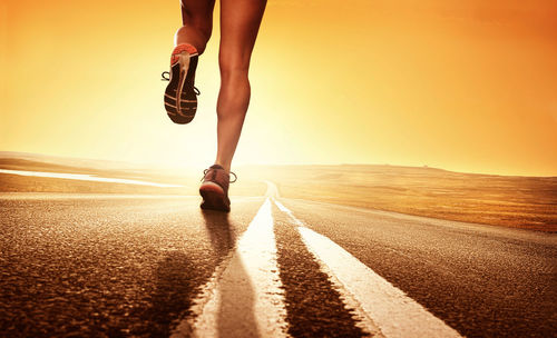 Low section of woman running on road at sunset