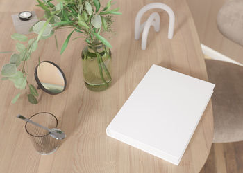 White book cover mock up with vase and other home accessories on wooden table. blank template