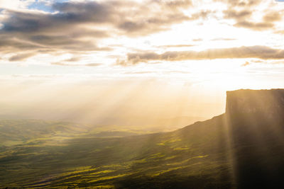 Sunlight streaming through clouds over landscape