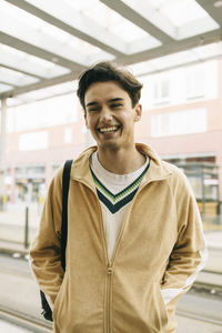 Happy young man with hands in pockets while standing at train station