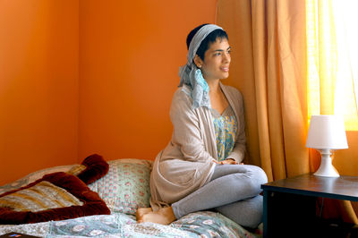 Full length of woman sitting by window on bed at home