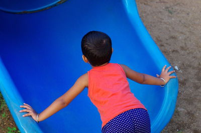 High angle view of girl bending on blue slide at playground