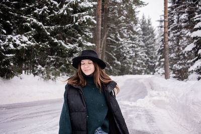 Smiling woman wearing hat standing on snow covered land during winter