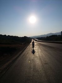 Silhouette man riding bicycle on road against sky