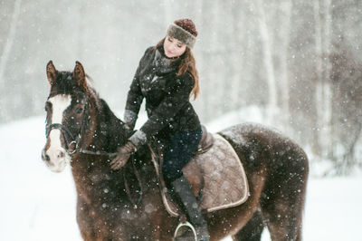 Beautiful woman riding horse on snow covered field