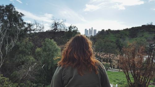 Rear view of woman standing by trees against sky