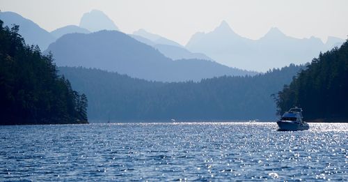 Boat sailing on lake by mountains against clear sky