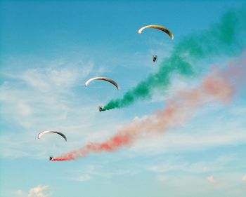 Low angle view of people paragliding against sky