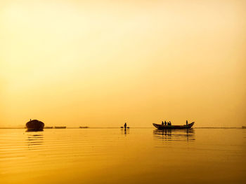 Silhouette people on boat in sea against clear sky during sunset