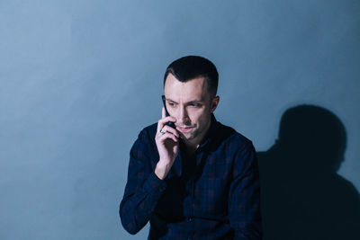 Man talking on mobile phone against wall