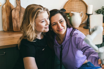 Girlfriends laugh merrily and take selfies in the kitchen.