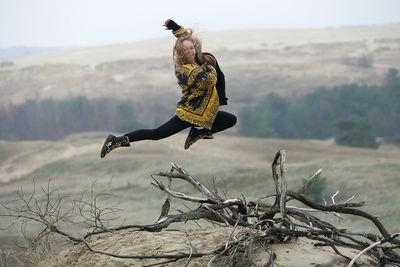 Cheerful woman jumping over broken branches at mountain