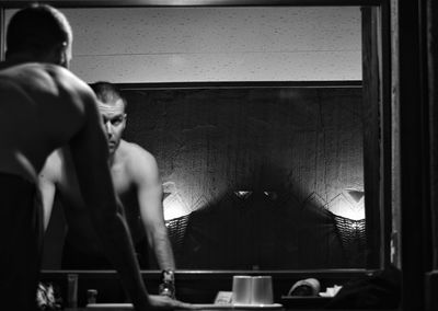 Shirtless man reflecting on mirror in bathroom at hotel