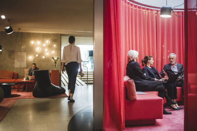 Full length of businesswoman walking in corridor while colleagues discussing in office