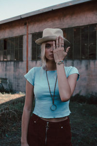 Portrait of young woman wearing hat standing against built structure