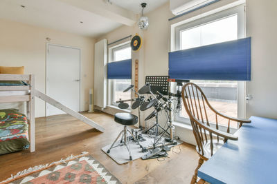 Electronic drum set placed near window in modern room with bunk bed and table with chair in loft style apartment