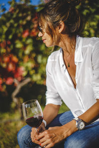 Woman in sunglasses having red wine against plants