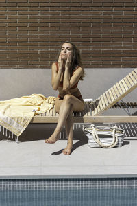 Vertical view of young woman spreading sun cream on her face while in the swimming pool lounge area