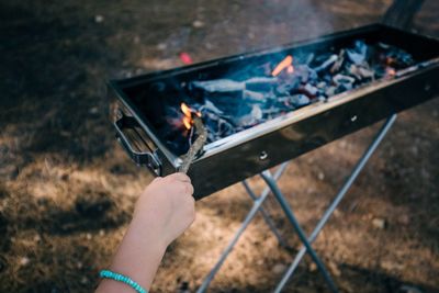 Cropped image of hand holding stick on barbecue grill